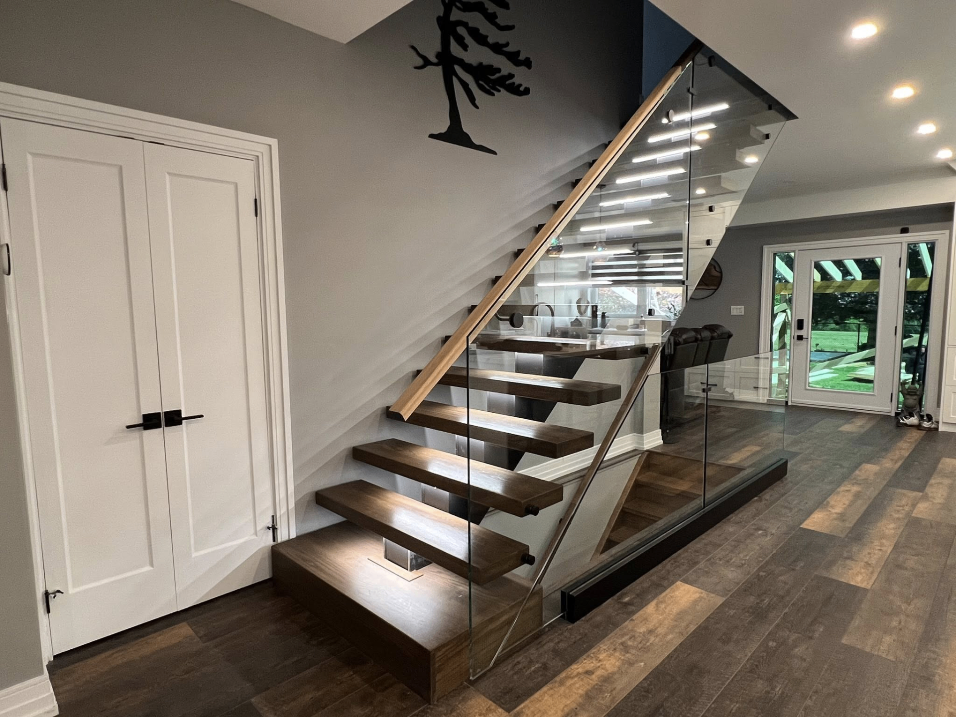 Floating open-riser staircase with wood treads, blackened steel stringer, and frameless glass railing